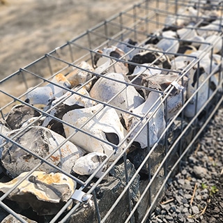 白〜灰色の自然石を詰めたガビオン（蛇篭）のクローズアップ。砕石敷きの上に据えられた鉄線メッシュ製の石籠。