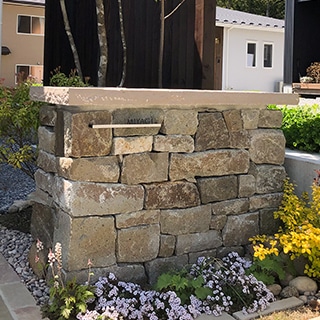 住宅庭の石積み門柱。不規則な自然石を積み上げ、平らな笠石を載せた外構の石工事例。